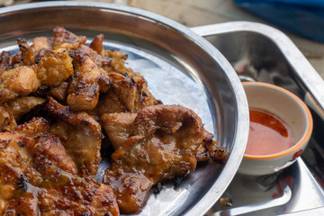 Thai grilled pork neck on a stainless steel tray with dipping sauce