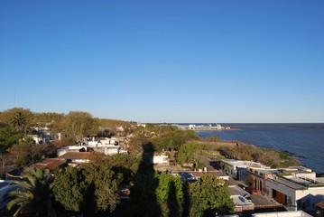 Obraz premium Ciudad, arboles y rocas cerca al mar, cielo despejado. 