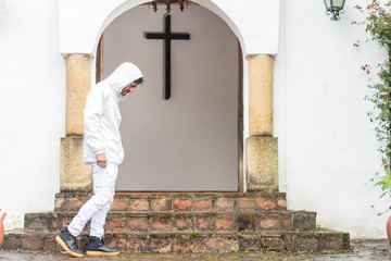Obraz na płótnie Canvas Young man with white hood walking in front of a christian old church entrance