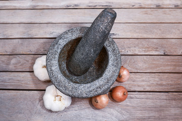 A mortar and pestle with garlic and onion isolated on wooden background.  Essential kitchenware to...