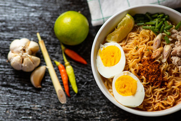 Spicy instant noodles soup with ingredient in bowl on wood black background