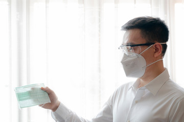 Asian man wearing safety google and N95 surgical mask to protect COVID-19 look at hygienic mask....