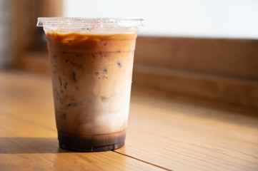 Iced caramel macchiato in plastic take away cup on wooden table near the window in the morning with copy space.