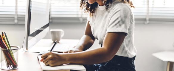 Portrait of african american black woman relaxing using technology of desktop computer while sitting on table.Young creative african girl working and write on book at home.work from home concept