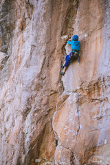 A woman in a helmet climbs a beautiful orange rock.