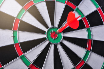 Red dart arrow hitting in the target center of dartboard