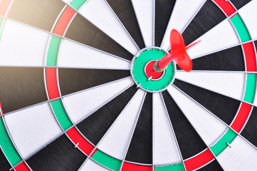 Red dart arrow hitting in the target center of dartboard