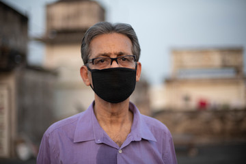 Fototapeta na wymiar portrait of an Indian old man with corona preventive mask on a rooftop during sunset in home isolation.Indian lifestyle, disease and home quarantine.