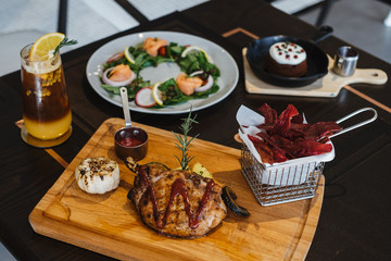 grilled pork chop with raspberry sauce and grilled garlic, potato, pumpkin vegetable on wooden board served with potato chips in basket. with salmon salad and orange mix cold brew coffee on table.
