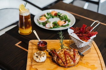 grilled pork chop with raspberry sauce and grilled garlic, potato, pumpkin vegetable on wooden board served with potato chips in basket. with salmon salad and orange mix cold brew coffee on table.
