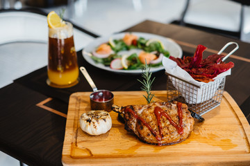grilled pork chop with raspberry sauce and grilled garlic, potato, pumpkin vegetable on wooden board served with potato chips in basket. with salmon salad and orange mix cold brew coffee on table.