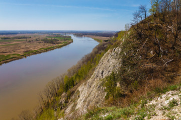 Top view of the bend of the river, two banks, bare branches against the blue sky on a spring day