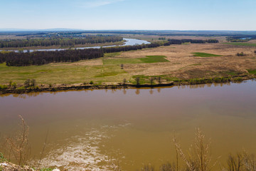 Top view of the bend of the river, two banks, bare branches against the blue sky on a spring day