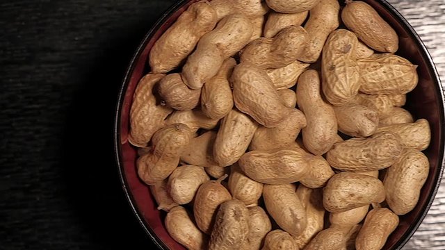 Top view of raw peanuts in a shell filled in a ceramic bowl on a dark table.