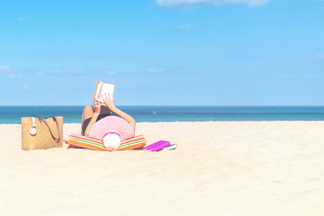 Sexy young woman lying on beach, reading book, relaxing on sand. Russian woman in bikini and sun hat, relaxing at sunny, blue sky clear water, remote tropical beaches and countries, travel concept.
