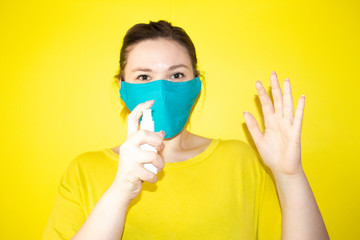 Portrait of young woman in protective mask with sanitizer gel on  yellow background. Coronavirus and health self isolation care concept.