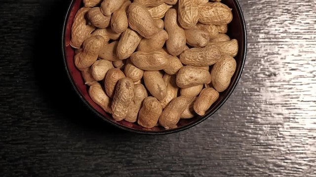 Top view of raw peanuts in a shell filled in a ceramic bowl on a dark table.