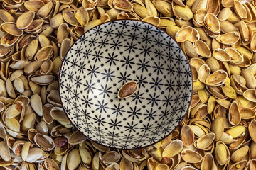 The last pistachio nut remained in a bowl. Around the bowl is a large pile of husks. Delicious nuts...