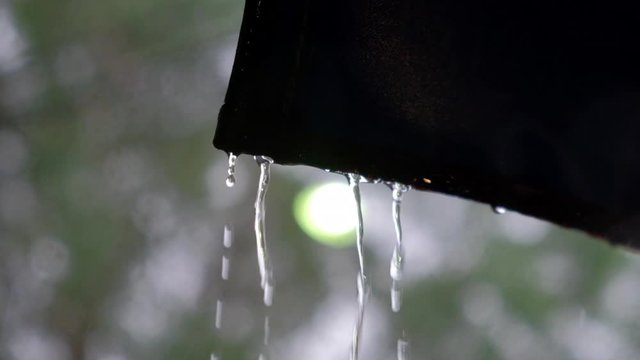 Rainwater dripping from an old rusty zinc roof during a heavy tropical rainstorm.