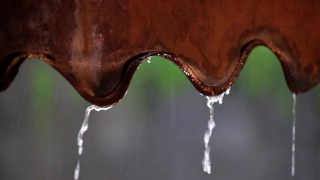 Rainwater dripping from an old rusty zinc roof during a heavy tropical rainstorm.