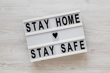 'Stay home stay safe' words on a lightbox on a white wooden background, top view. Overhead, from above, flat lay.