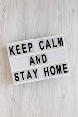 'Keep Calm and Stay Home' words on a modern board on a white wooden surface, top view. Overhead, from above, flat lay.