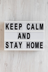 'Keep Calm and Stay Home' words on a lightbox on a white wooden surface, top view. Overhead, from above, flat lay.