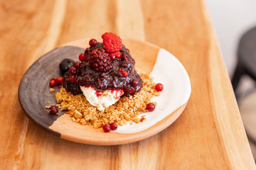 Semi frozen mix berry (blackberry and raspberry) cheesecake with crushed almond crumble. Served in three colors (brown, light orange and white) ceramic plate.