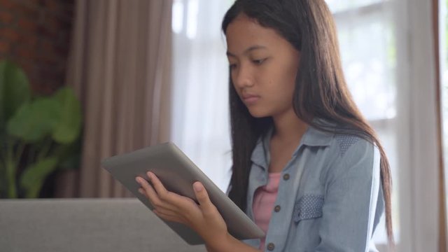serious looking teen using tablet at home while sitting on a couch