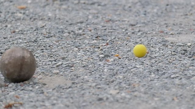 Close up of petanque boules and a yellow jack on the gravel ground.