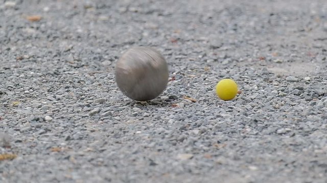 Close up of petanque boules and a yellow jack on the gravel ground.