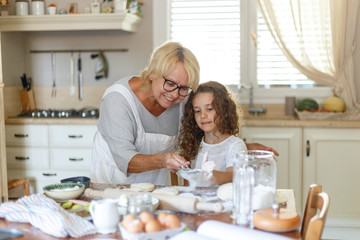 A grandmother and niece is cooking. A smiling grandmother is cooking a cookies. Stay home and cook with your loved ones.