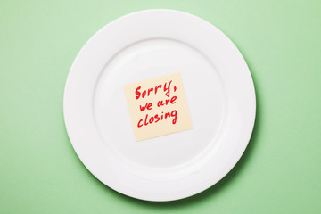 Note with text in a white plate on a green background, top view. Concept on the topic of closing the restaurant business in connection with the covid-19 pandemic