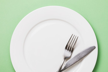 Empty white plate and cutlery on a green background, top view