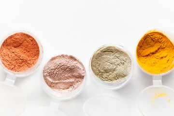 A top view of the loose pigments and powders in circle plastic jars on white background. Food and cosmetic colorful organic ingredients. Close-up