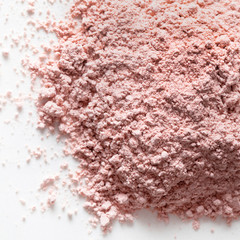 A pile of loose peach pink powder pigmant for cosmetic or make-up on white background. Texture. Close-up. Top view