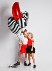 Two nice smiling kids girls in skirts and t-shirts with big air balloons stand together hugging  