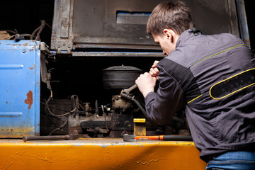 Fototapeta na wymiar A male mechanic is repairing the engine of an old truck with an open hood with a wrench. Auto service industry.