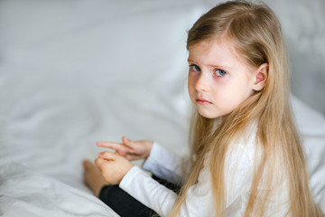 A little girl with long blond hair is sad and crying at home. The child is upset.