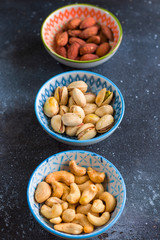 Nuts in bowls on the table, almonds, cashews and coasted nuts on the blue background.