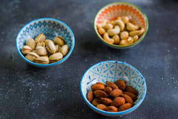 Nuts in bowls on the table, almonds, cashews and coasted nuts on the blue background.