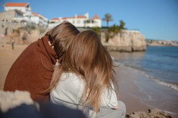 Fototapeta na wymiar Portugal Lisbon two girls on the beach cuddle turning their hair to the viewer