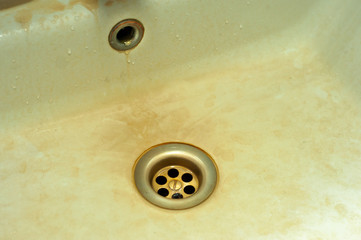 Brown stains and sediment around the washbasin drain. Dirty stains from hard water and excess iron.