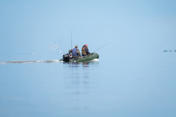Two fishermen motoring infladable boat with outboard motor on the very calm lake with infinite...