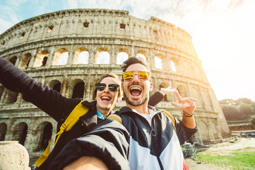 Happy caucasian couple is taking a selfie smiling at the camera in front of the colosseum in Rome	