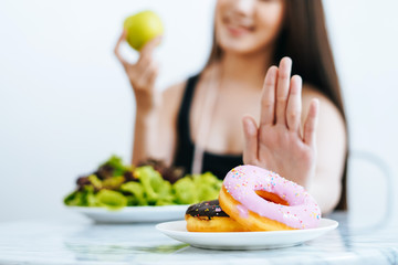 Close up female hand while pushing out her favorite donut and choose green apple and vegetables for good health. Diet and healthy concept