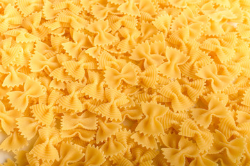 Heap of dried Farfalle Rigate Italian pasta ready to be cooked, isolated on a white table, top view or flat lay of healthy food 
