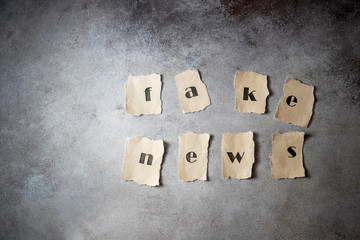 Fake news concept, letters written on old paper, on gray concrete background. Social media concept.