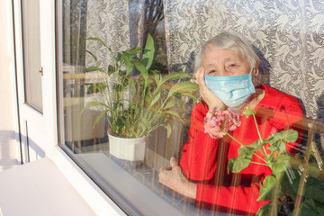 Fototapeta premium The Covid-19, health, safety and pandemic concept - senior old lonely woman sitting near the window