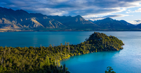 Green lush Forest peninsula on Lake Wakatipo with Southern Alps mountains in the background, aerial...
